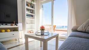 Un salon moderne comprenant un canapé, une table basse avec un vase de fleurs, une bibliothèque et un téléviseur.