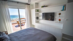 Une chambre avec un lit, un téléviseur fixé au mur et une vue sur la mer, accessible par une porte coulissante.