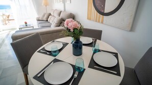 Un coin repas avec une table ronde dressée pour quatre personnes, agrémentée d’assiettes blanches, de verres bleus et d’un vase rempli de fleurs.