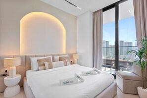 Una habitación de hotel moderna con una cama grande, dos mesitas de noche con lámparas, vistas a la ciudad y una planta en maceta.