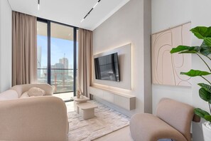 Un salon moderne doté d’un grand téléviseur, de sièges confortables, d’une vue sur la ville et d’un balcon agrémenté d’une plante.