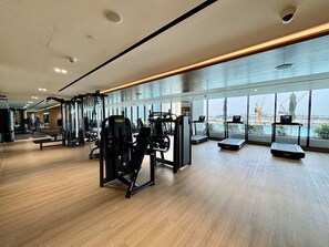 Ein modernes Fitnessstudio mit unterschiedlichen Trainingsgeräten, großen Fenstern und Holzboden.