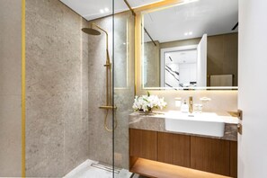 Un baño moderno con ducha envuelta en cristal, pared de azulejos de mármol, tocador de madera y un espejo grande.