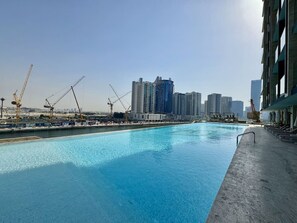 Ein Schwimmbad mit Stadtansicht im Hintergrund, darunter Hochhäuser und Baukräne.