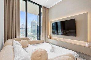 Une chambre d’hôtel moderne dotée d’un grand lit, d’un téléviseur à écran plat fixé au mur et offrant une vue sur la ville grâce à de grandes fenêtres.