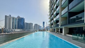 A modern hotel with a rooftop pool, high-rise buildings in the background, and a clear sky. - Exclusive 1 Bedroom  in Trillionaire Residences (Dubai)