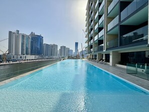 Un hotel moderno con piscina en la azotea y rascacielos al fondo, bajo un cielo despejado.