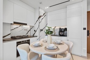 Una cocina moderna con armarios blancos, salpicadero de mármol y un comedor con una mesa redonda para dos personas.