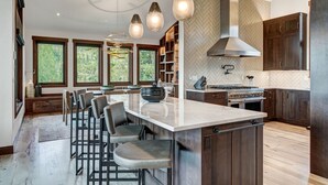 A modern kitchen with a large island, bar seating, and a view of the outdoors through large windows.