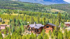 A lodge with a modern design, surrounded by dense forest and mountains in the background.