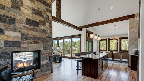 A modern kitchen with a stone wall, wooden beams, and large windows.