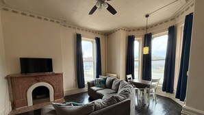 A living room with a fireplace, two sofas, a dining table with chairs, and large windows with curtains. - Shearer Historical House Unit 1 (Bay City)