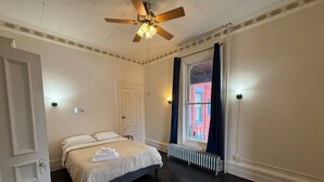 A bedroom with a bed, a ceiling fan, a radiator, and a window with curtains. - Shearer Historical House Unit 1 (Bay City)