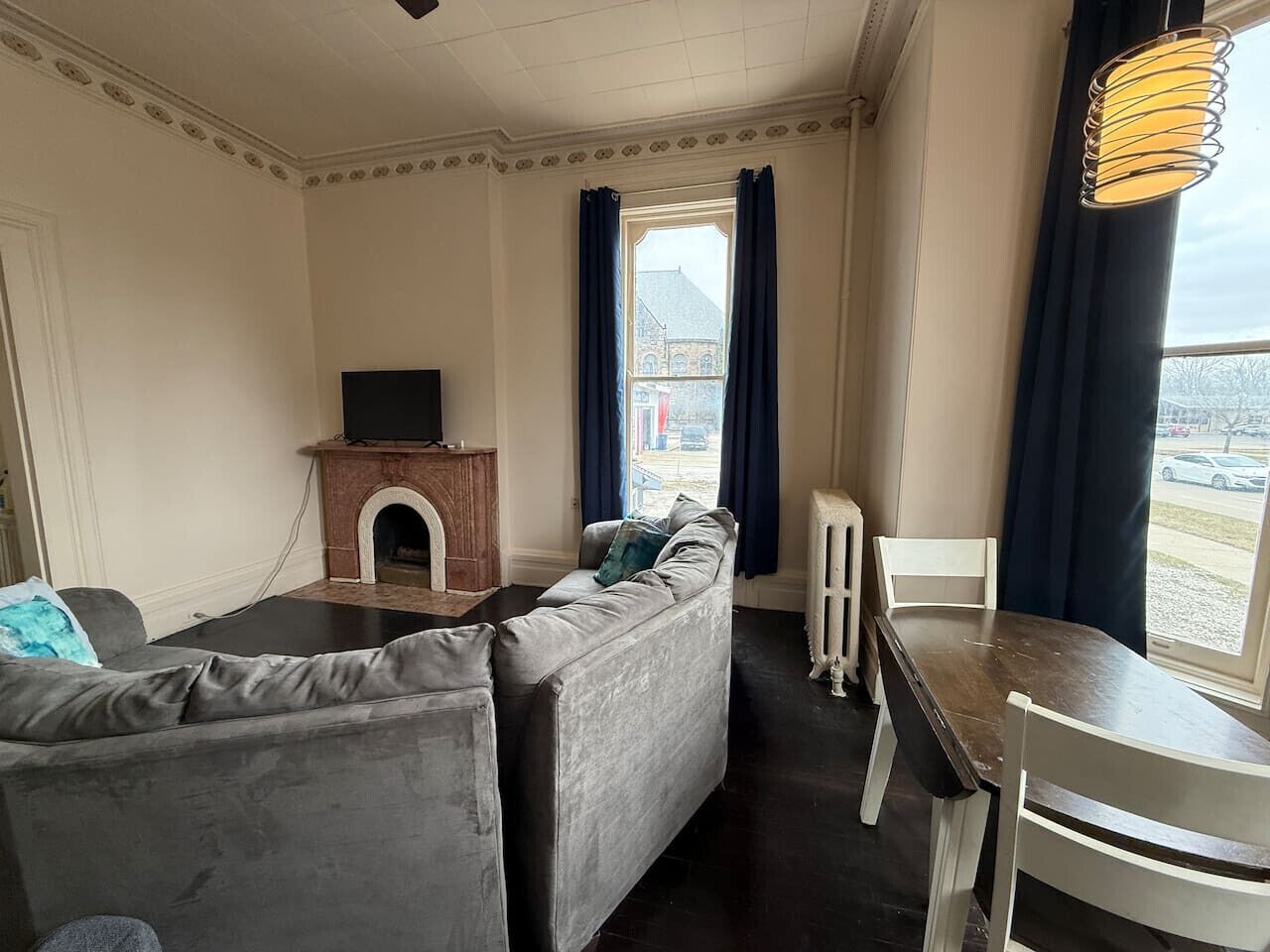 Ein Wohnzimmer mit Kamin, einer Couch, einem Esstisch mit Stühlen und Blick auf ein Gebäude durch ein Fenster.