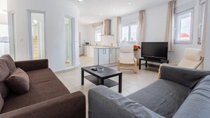 Un salon moderne avec un canapé, une table basse, un téléviseur et un coin repas, la cuisine étant visible au fond.