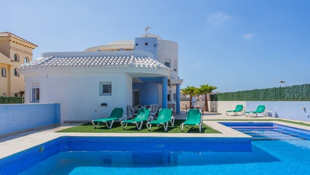 Une villa moderne dotée d’une piscine, de fauteuils de jardin verts et surplombant un ciel d’un bleu limpide.