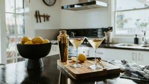 Een aanrecht met een schaal citroenen, een cocktailshaker en twee martini glazen.