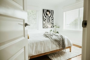 Ein Schlafzimmer mit einem Bett, einem zebrastreifenartigen Kunstwerk und einem Fenster mit Jalousien.
