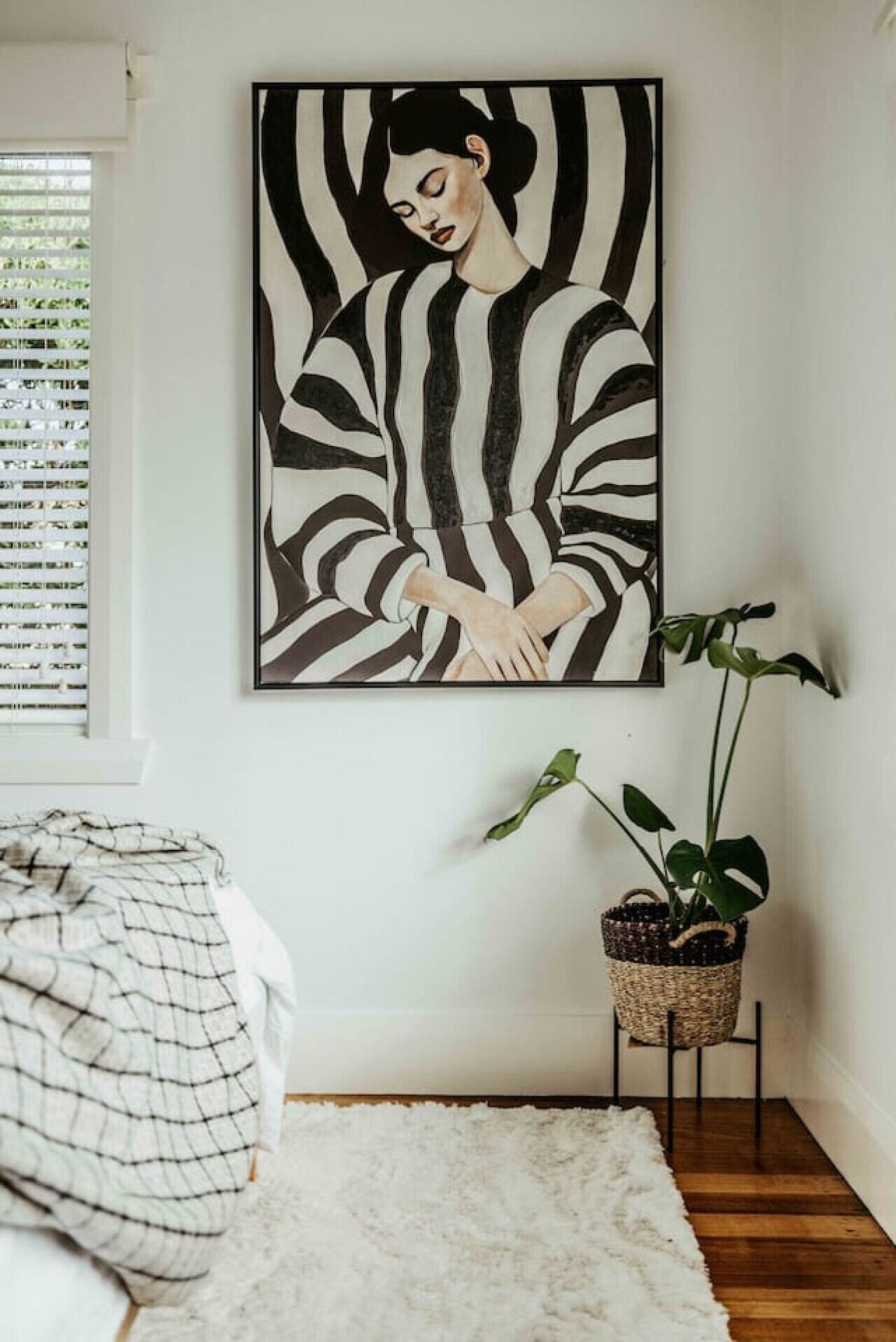 A bedroom with a bed, a white rug, a potted plant, and a large abstract painting on the wall.