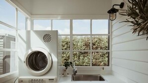 Een wasruimte met een voorlader wasmachine en droger, een wasbak en een raam met uitzicht op bomen.