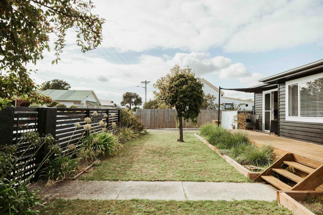 A residential backyard with a wooden deck, a small tree, and a house with a modern design.