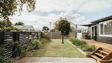 A residential backyard with a wooden deck, a small tree, and a house with a modern design.