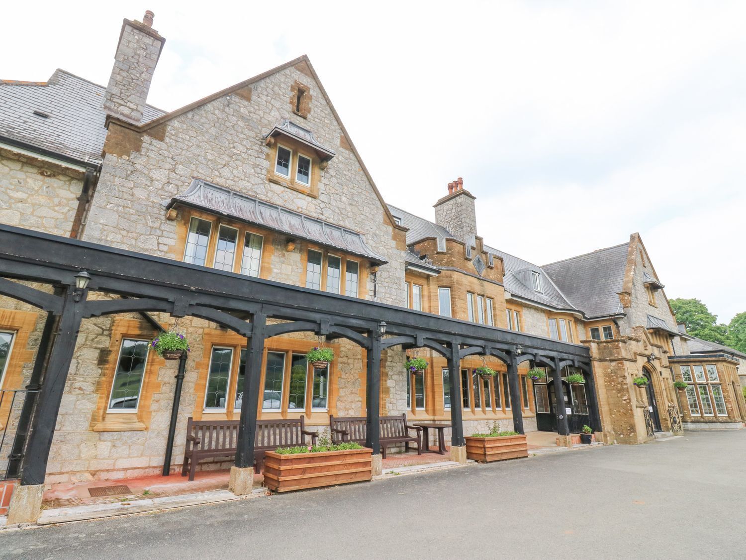 A stone building with a covered walkway, wooden benches, and hanging flower baskets.