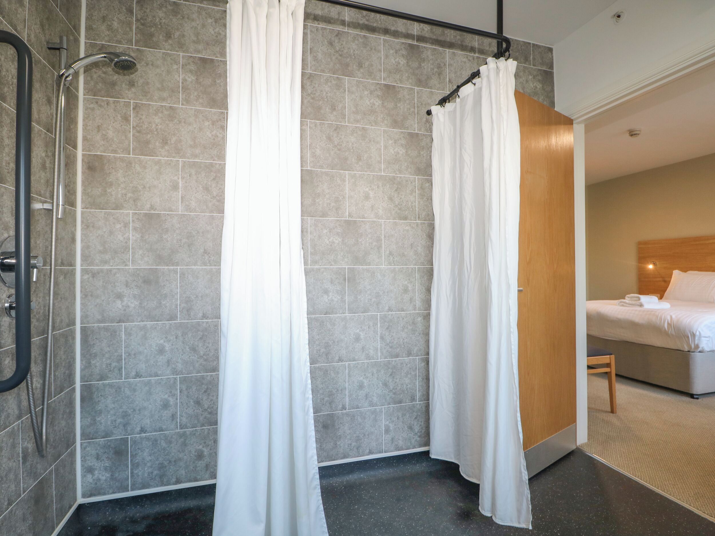 A modern bathroom with a shower, a toilet, and a bed with a wooden headboard.