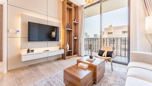 Una sala de estar moderna con televisor de pantalla plana, estanterías de madera, una mesa de centro, un sofá y un balcón con vista a la ciudad.