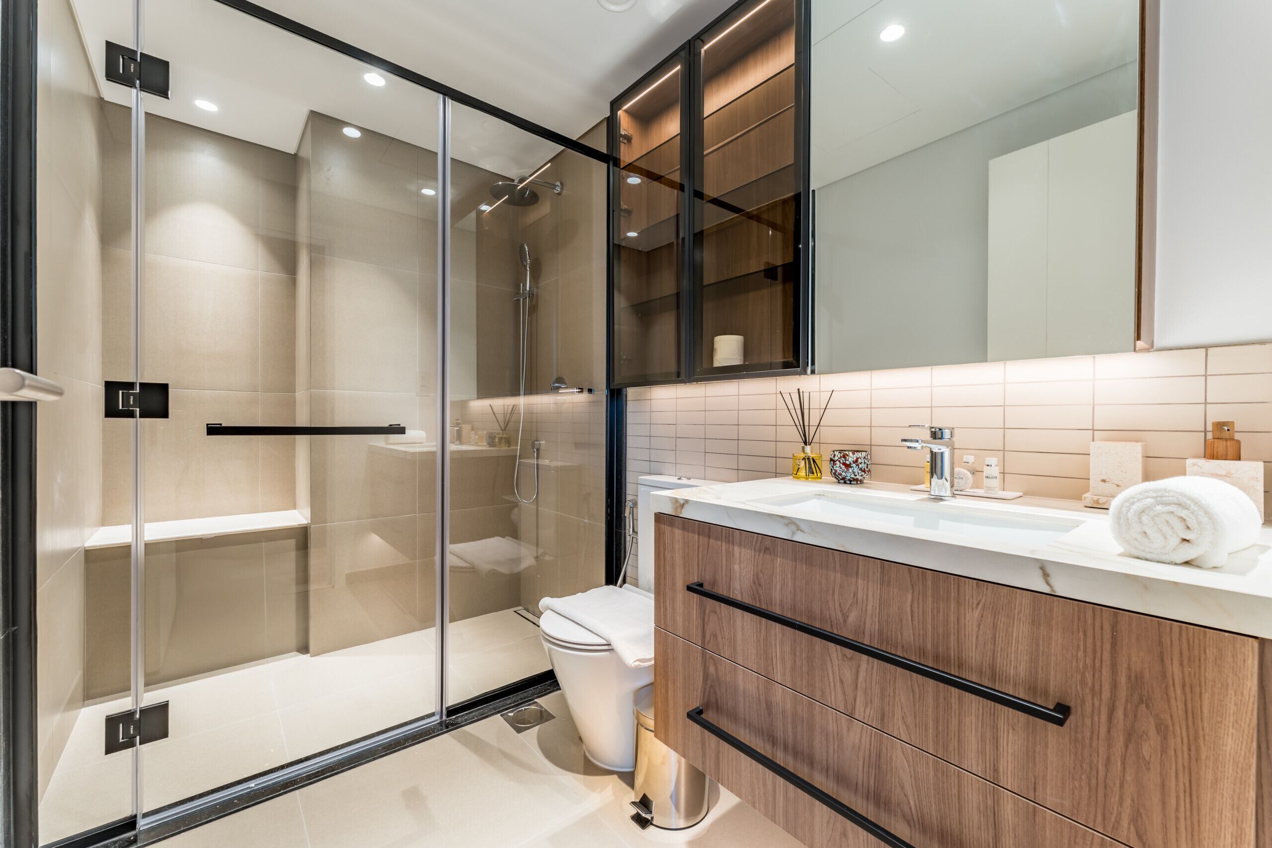 A modern bathroom with a glass-enclosed shower, a white toilet, and wooden cabinets.