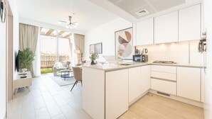 A modern kitchen with white cabinetry, a central island, and a dining area with a view of the outdoors. - New 1 BR with 2 Balconies Near Circle Mall Luma22 West Tower (Dubai)