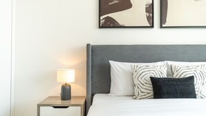 A neatly arranged bedroom with a bed, bedside table, lamp, and artwork on the wall. - New 1 BR with 2 Balconies Near Circle Mall Luma22 West Tower (Dubai)