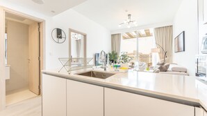 A modern kitchen with a central island, a dining area with a sofa, and a large window with curtains. - New 1 BR with 2 Balconies Near Circle Mall Luma22 West Tower (Dubai)
