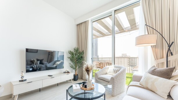 A modern living room with a flat-screen TV, a glass coffee table, a sofa, and a chair. There is a balcony with a view of the city. - New 1 BR with 2 Balconies Near Circle Mall Luma22 West Tower (Dubai)