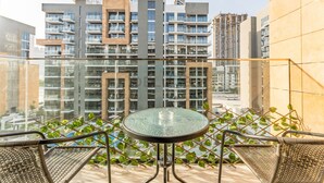 A balcony with a glass table and wicker chairs, overlooking a modern high-rise building with multiple balconies. - Studio with Pool and Community View, Near Soho Garden DXB and Meydan Golf Club (Dubai)