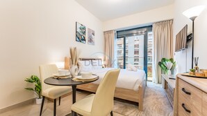 A modern hotel room with a bed, a dining table with chairs, a small desk, and a large window with curtains. - Studio with Pool and Community View, Near Soho Garden DXB and Meydan Golf Club (Dubai)