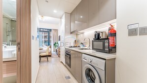 A modern kitchen with stainless steel appliances, a washing machine, and a fire extinguisher. - Studio with Pool and Community View, Near Soho Garden DXB and Meydan Golf Club (Dubai)
