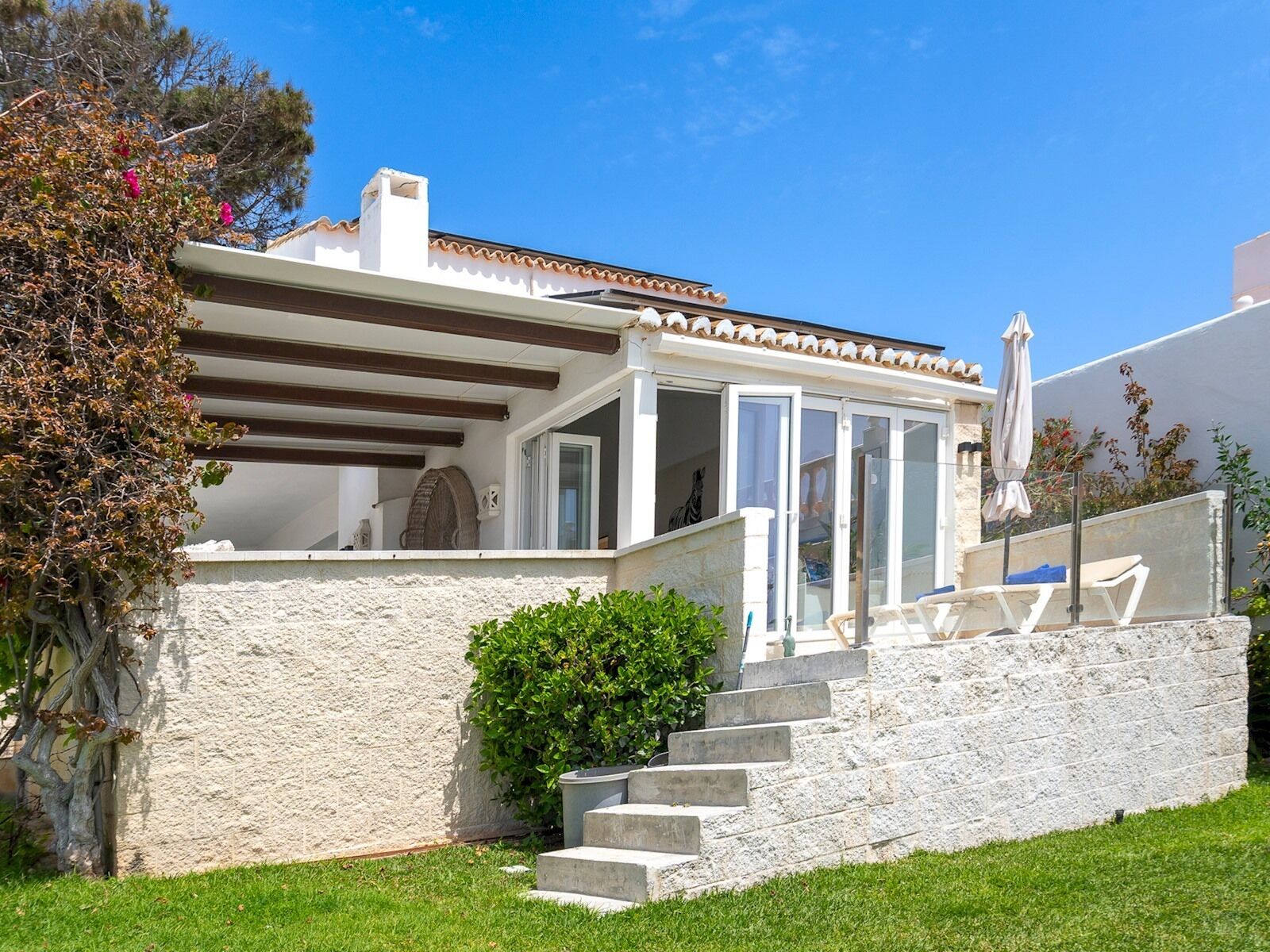 Une maison située sur la côte, dotée d’une façade en pierre, d’un patio couvert avec des meubles d’extérieur et offrant une vue dégagée sur la mer.
