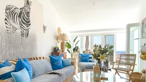 A living room with a wicker sofa, a glass coffee table, and a view of the sea through large windows.
