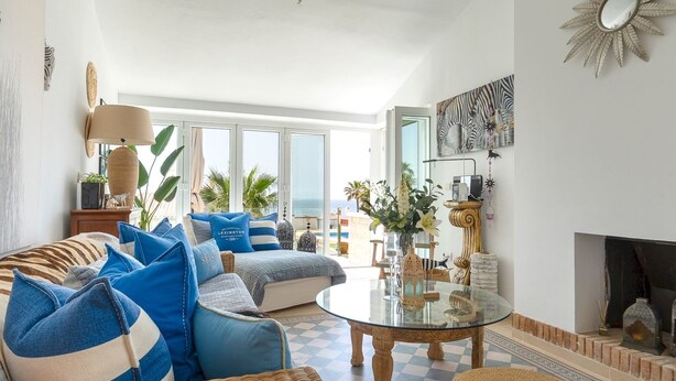 A spacious living room with a large sofa set, a glass coffee table, and a view of the sea through large windows.