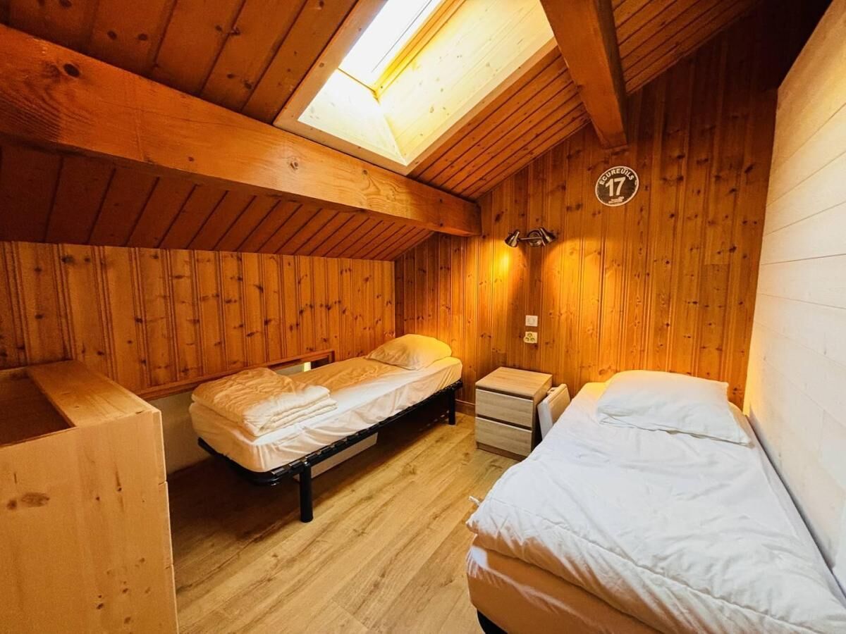 A cozy wooden room with two single beds, a small bedside table, and a skylight.