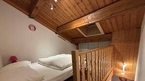 Ein Zimmer mit Holzboden, einem Bett mit weißer Bettwäsche, einer roten Lampe und einem Holzbalken.