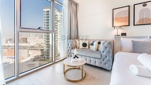 Una sala de estar moderna con un ventanal grande, un sofá gris, una cama blanca y una pequeña mesa redonda.