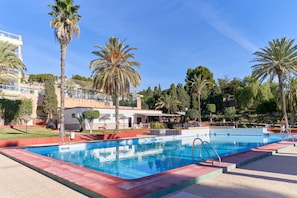 A swimming pool with a red border, surrounded by palm trees and a building with balconies.