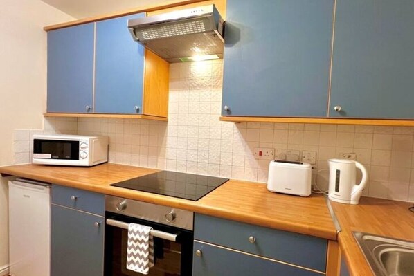 A compact kitchen with blue cabinets, a microwave, a toaster, and a kettle.