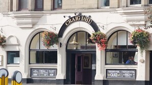 A building with a sign reading "CRAIG DHU" above the entrance. There are flower baskets hanging from the windows, and a sign below the entrance advertises a quiz event.