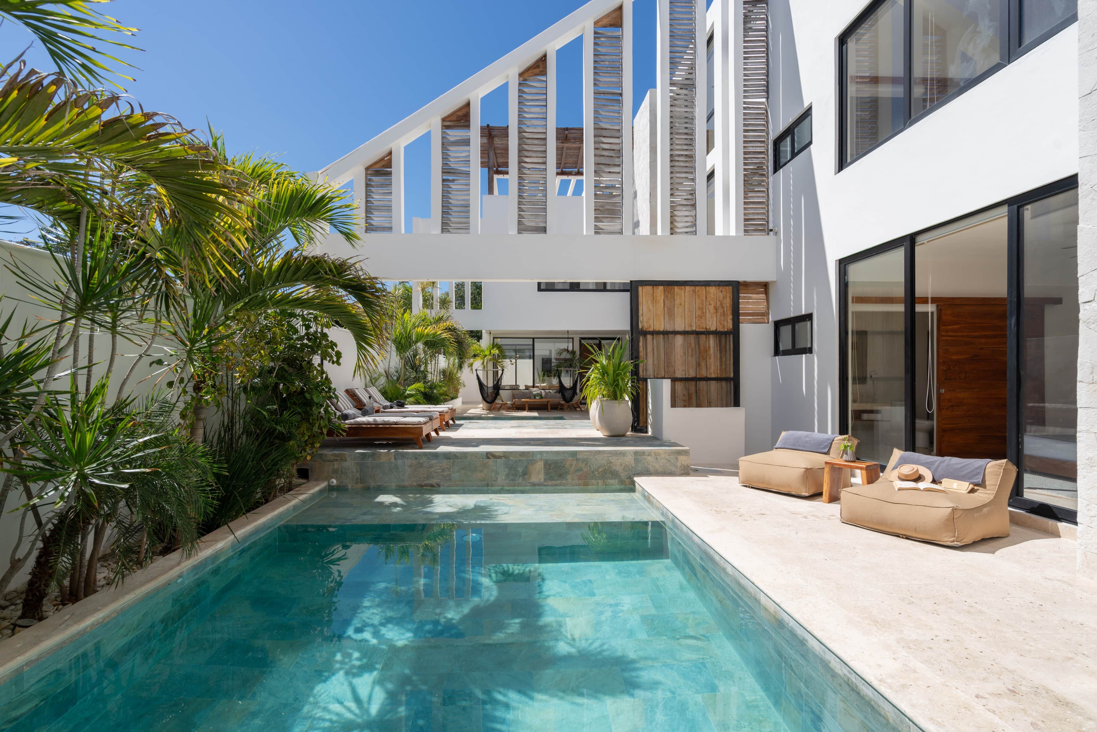 A modern poolside area with a clear pool, lounge chairs, and a large window overlooking the pool.