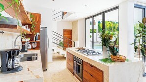 Une cuisine moderne dotée d’un îlot central, d’appareils électroménagers en acier inoxydable et offrant une vue sur l’extérieur.