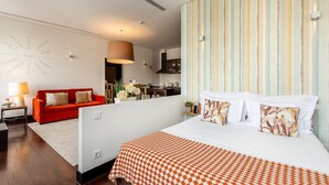 A hotel room with a large bed, a red sofa, a kitchen area, and a striped wall.