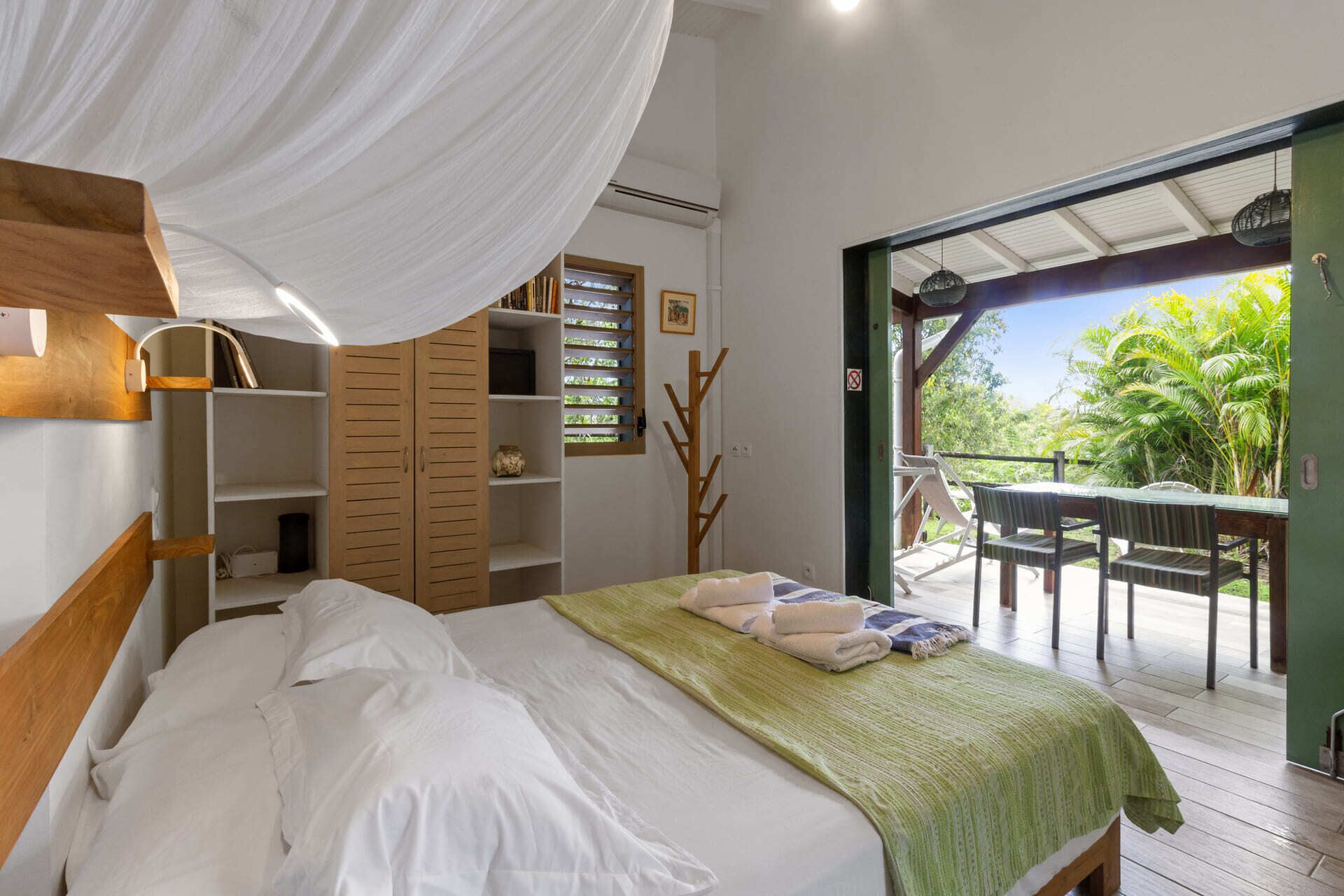 A bedroom with a canopy bed, wooden shelves, and a view of a patio with a table and chairs.